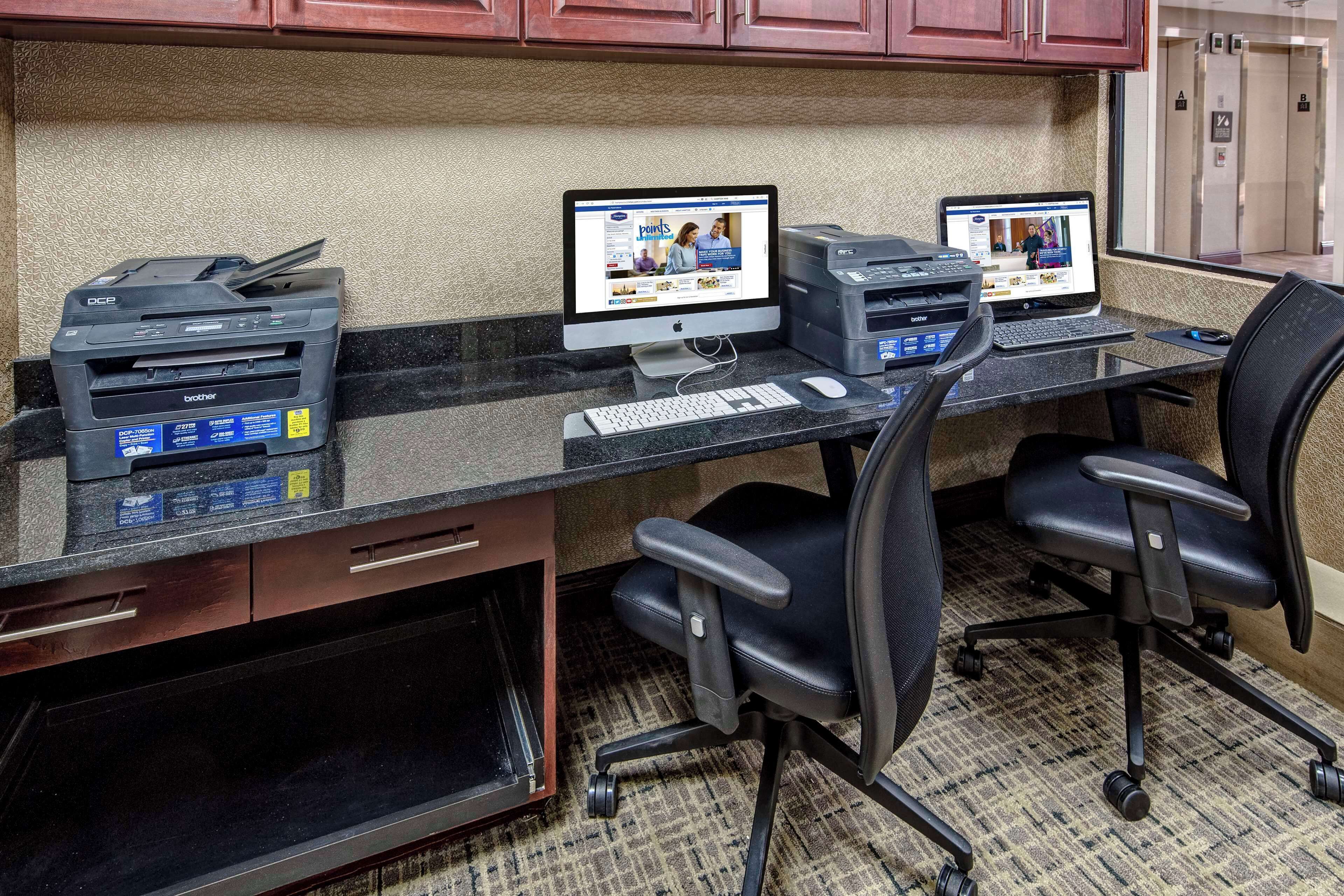 A workspace with two desktop computers, a printer, and a keyboard on a desk.
