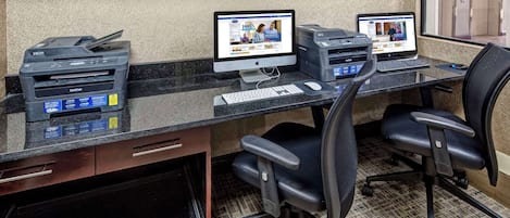 A workspace with two desktop computers, a printer, and a keyboard on a desk.