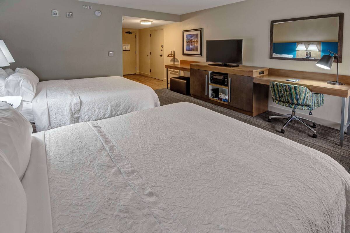 A hotel room with two beds, a desk, a television, and a chair.