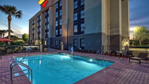 A hotel with a swimming pool, outdoor seating, and a palm tree. - Hampton Inn Orlando-Maingate South (Davenport)