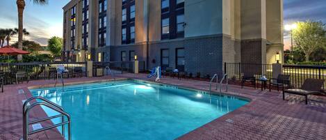 A hotel with a swimming pool, outdoor seating, and a palm tree.
