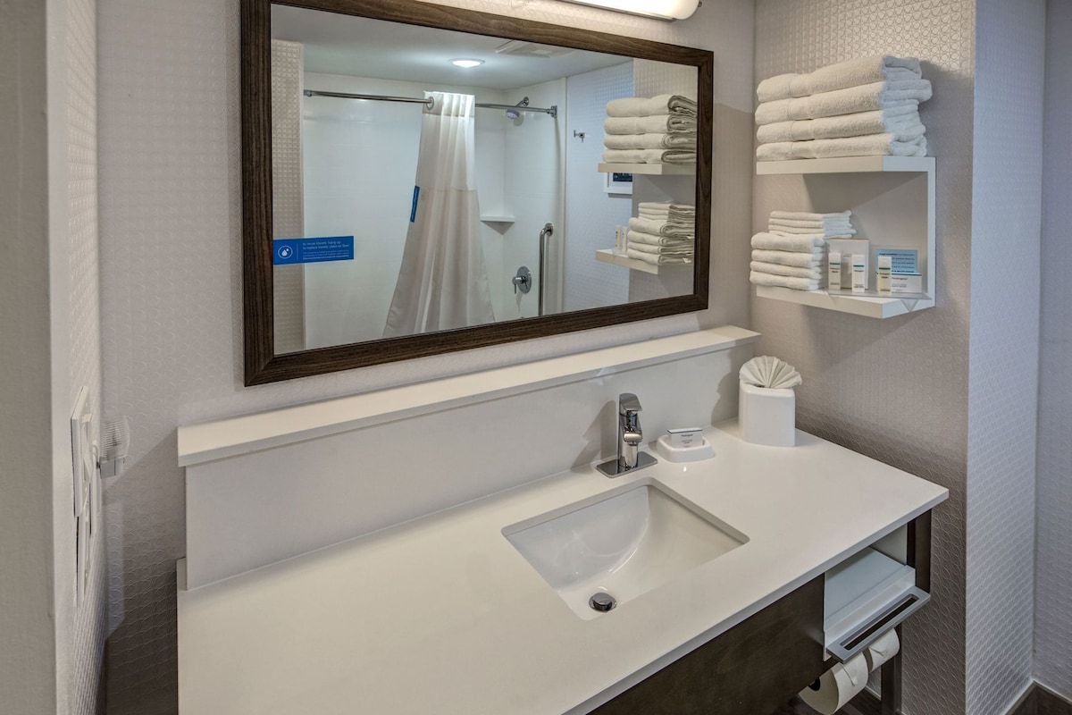 A bathroom with a sink, mirror, towel rack, and a shower curtain.