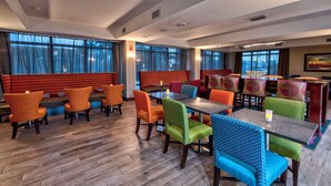 A hotel dining area with wooden flooring, multiple dining tables, and colorful upholstered chairs. - Hampton Inn Orlando-Maingate South (Davenport)