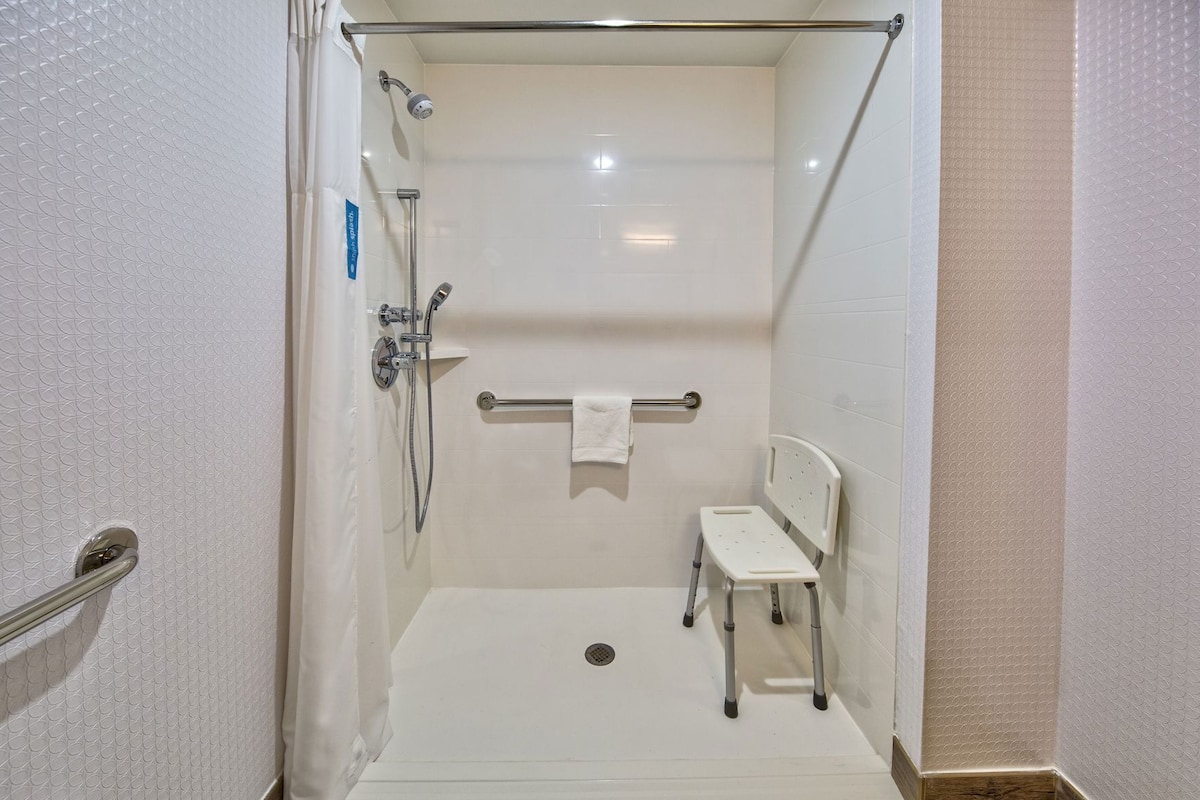 A walk-in shower with a handheld showerhead, a handheld shower attachment, a towel rack with a towel, and a small white chair.