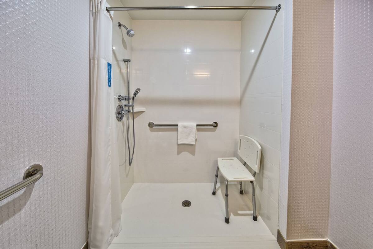 A walk-in shower with a handheld showerhead, a handheld shower attachment, a towel rack with a towel, and a small white chair.