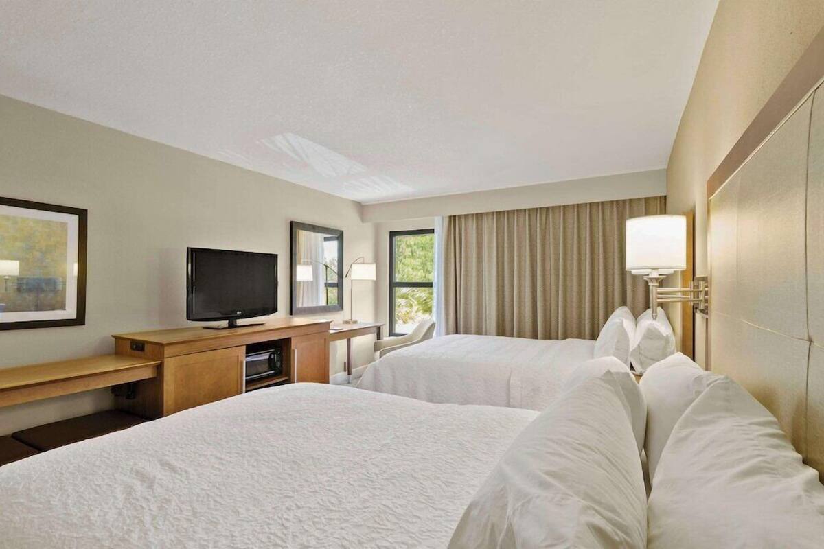 A hotel room with two beds, a desk with a television, a lamp, and a window with curtains.
