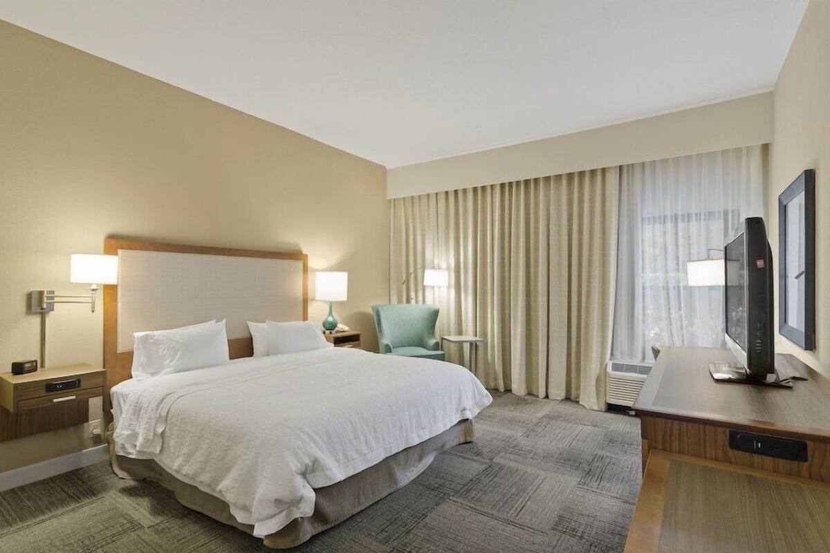 A hotel room with a large bed, two bedside tables with lamps, a television, and a window with curtains.