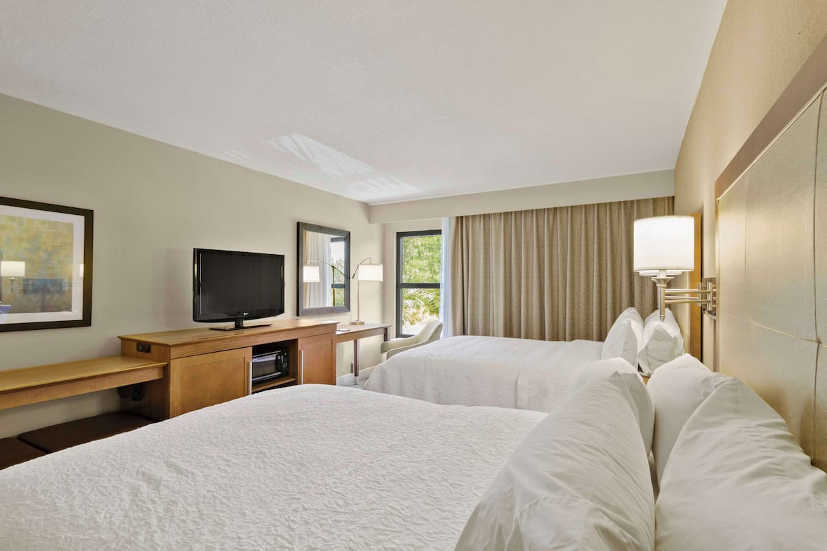 A hotel room with two beds, a desk with a television, and a window with curtains.