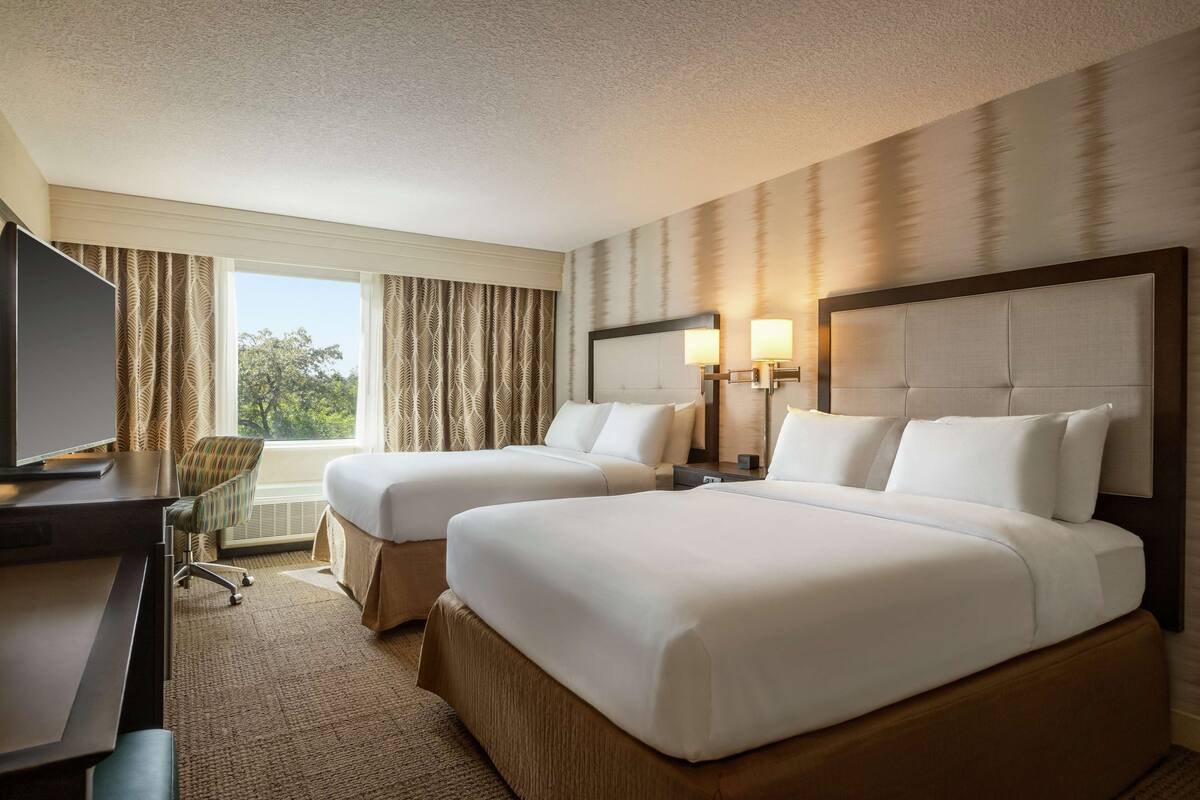A hotel room with two beds, a desk, a chair, and a TV.