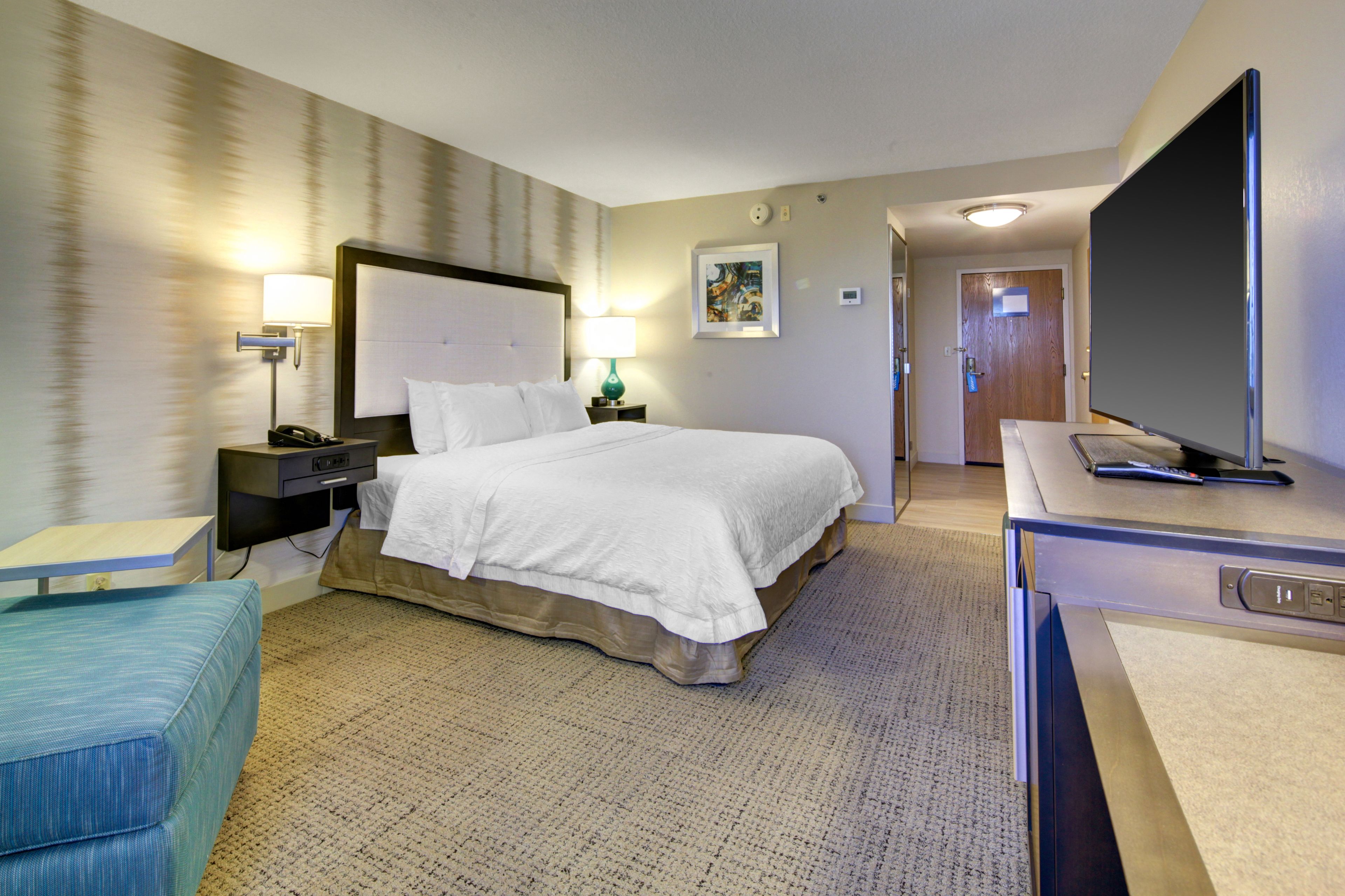 A hotel room with a bed, bedside tables with lamps, a television, and a small seating area.