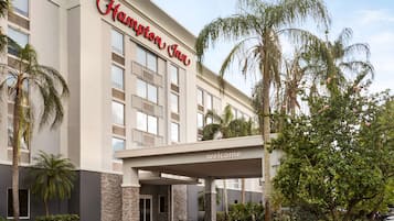 A Hampton Inn hotel with a modern facade, a welcoming entrance, and a landscaped outdoor area with palm trees and shrubs.