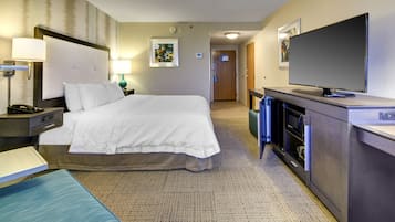 A hotel room with a large bed, bedside tables, a desk, a television, and a bathroom visible in the background.