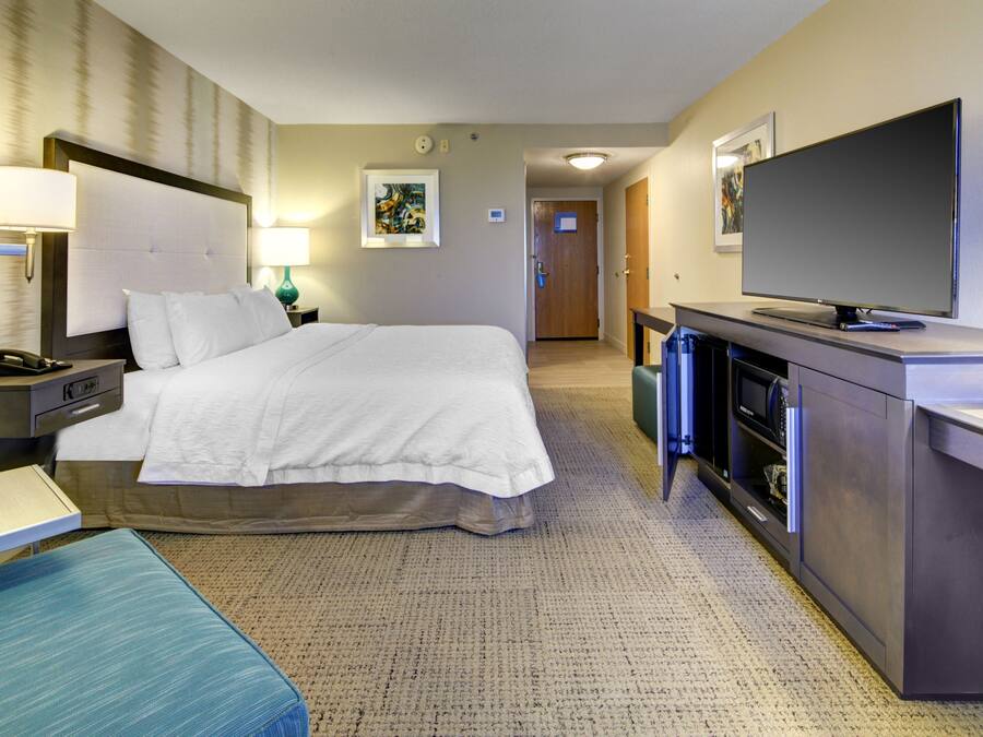 A hotel room with a large bed, bedside tables, a desk, a television, and a bathroom visible in the background.