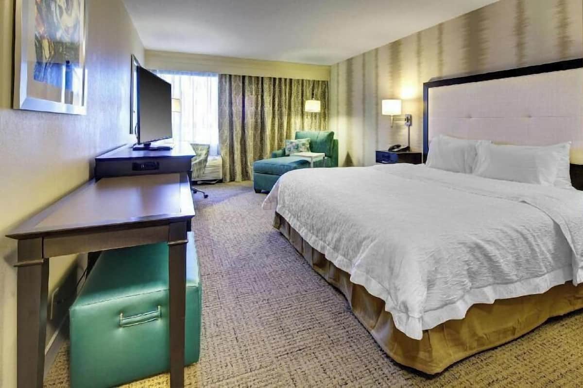 A hotel room with a bed, desk, chair, and a television.