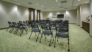 A conference room with rows of foldable chairs, a projector screen, and a framed picture on the wall.