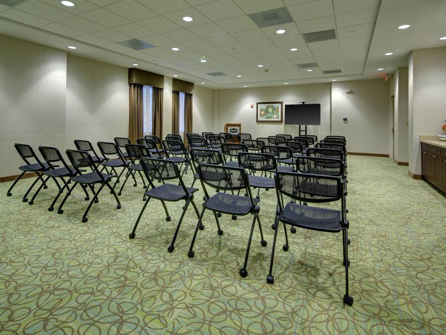 A conference room with rows of foldable chairs, a projector screen, and a framed picture on the wall.