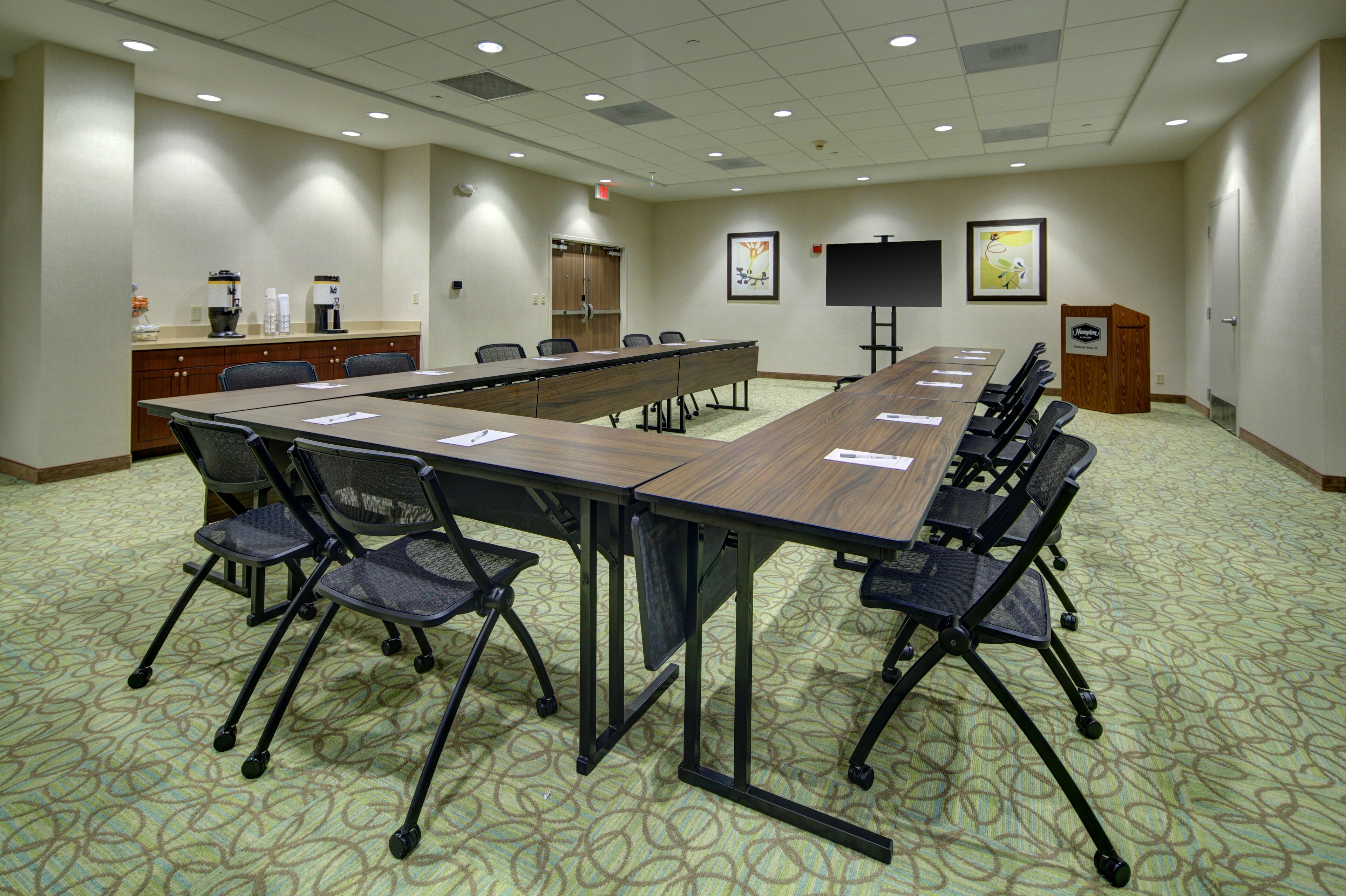 A conference room with a long table, chairs, a coffee station, and artwork on the walls.