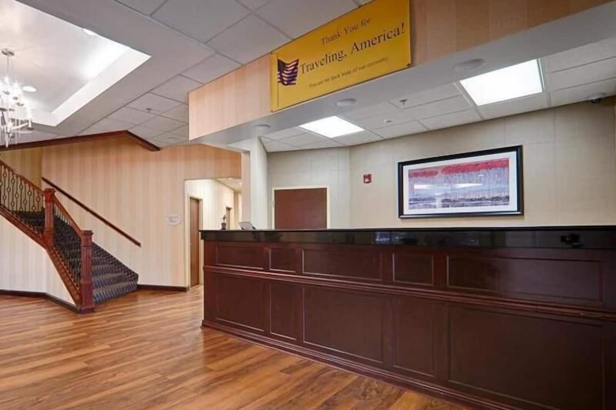 A reception desk with a wooden finish, a staircase with a wooden railing, and a framed picture on the wall.