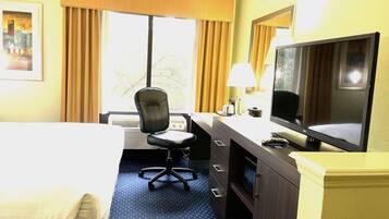 A hotel room with a bed, desk, chair, television, and a window with curtains.