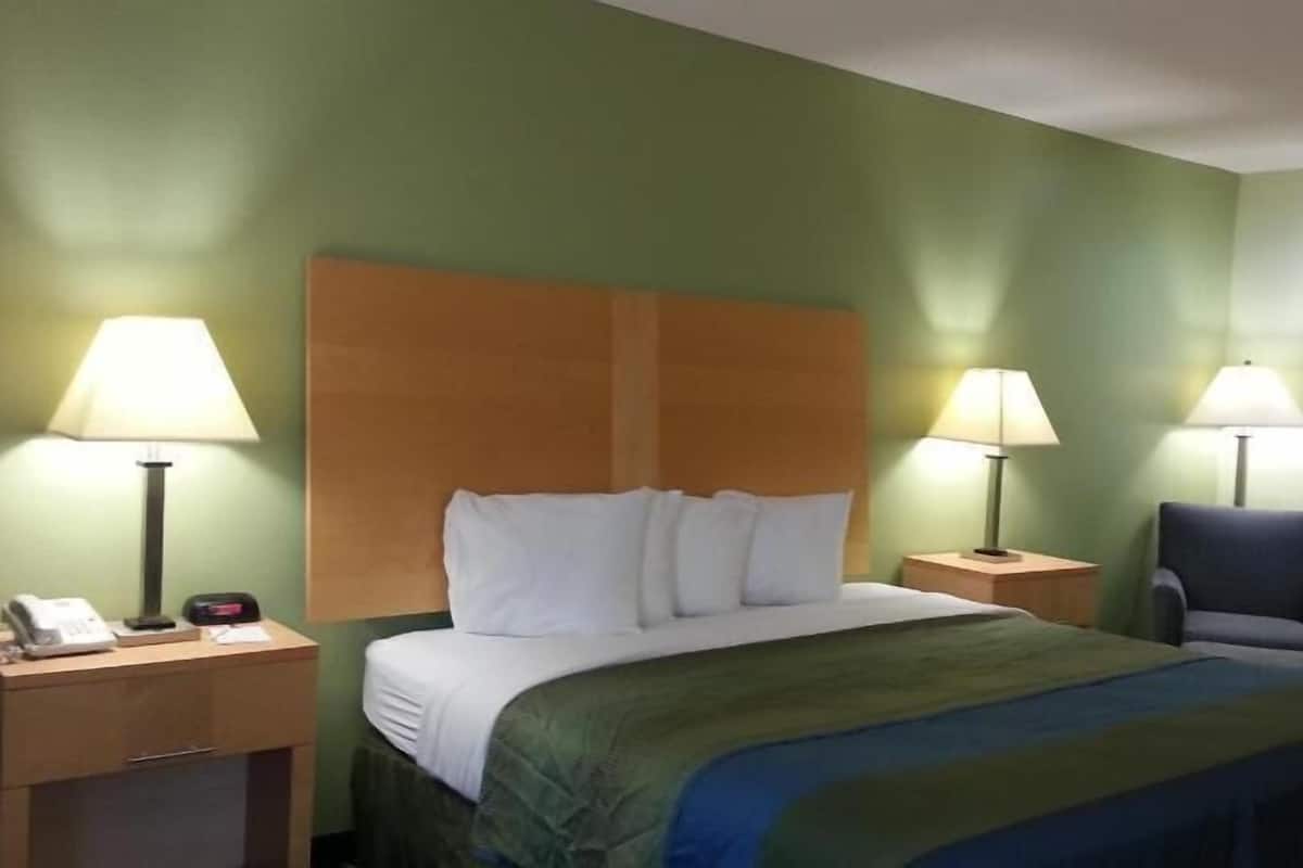 A hotel room with a bed, two bedside lamps, a chair, a nightstand, and a phone.