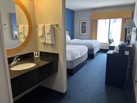 Habitación de hotel con baño, dos camas, un escritorio y una ventana.