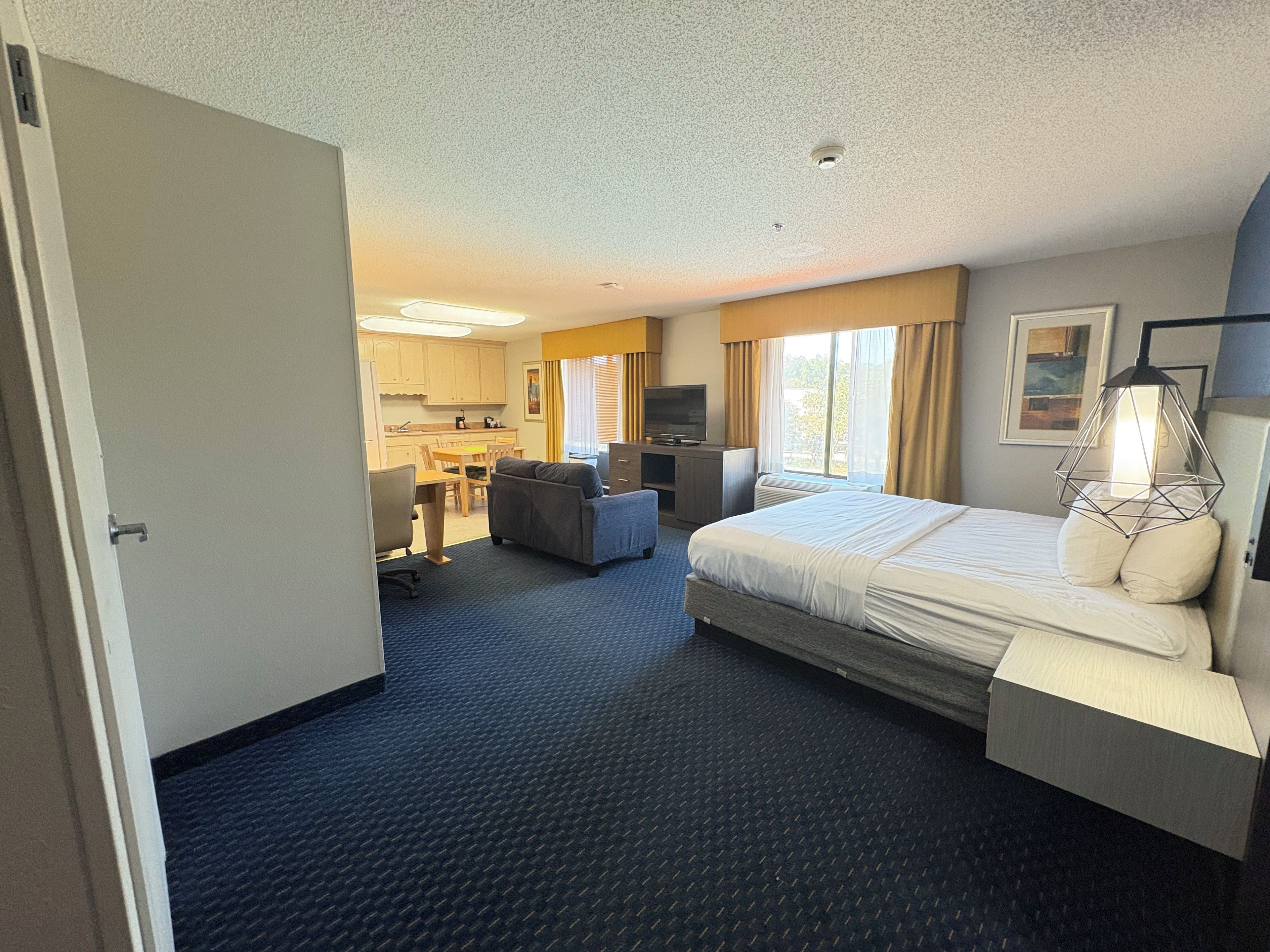 A hotel room with a bed, a desk, a chair, a television, and a kitchenette.