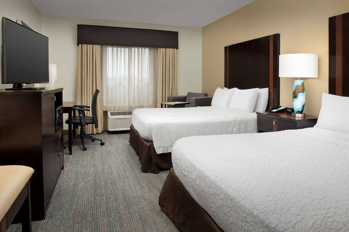 A hotel room with two beds, a desk, a TV, and a lamp.