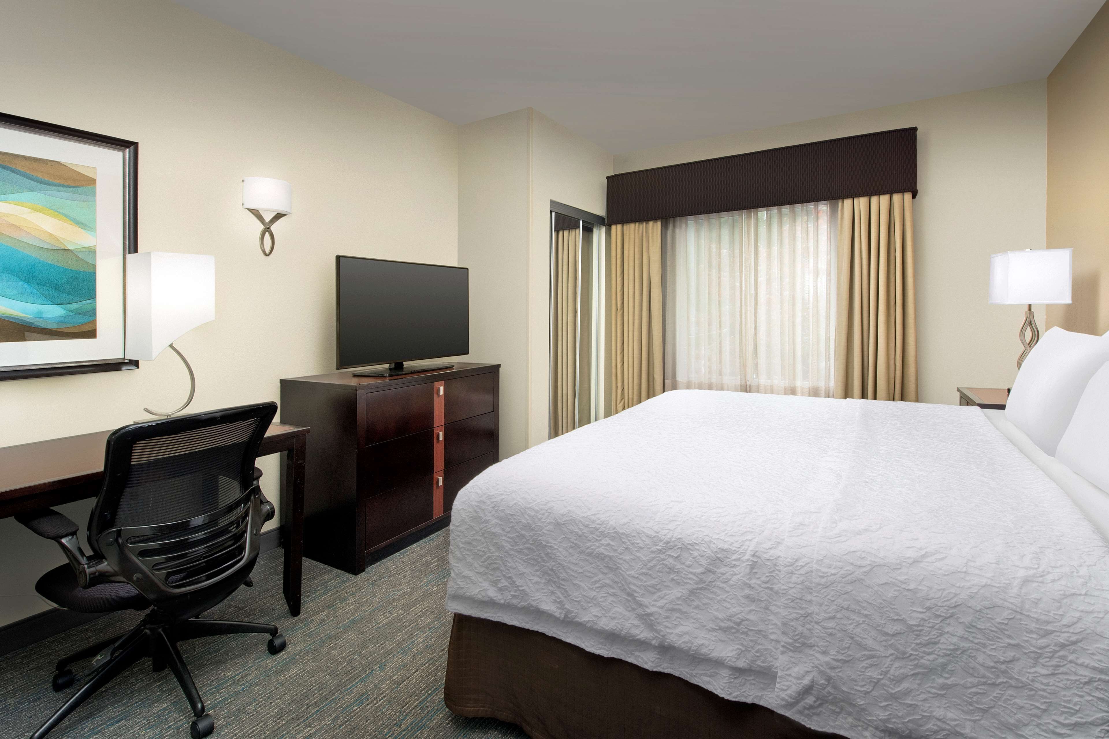A hotel room with a bed, desk, chair, television, and curtains.