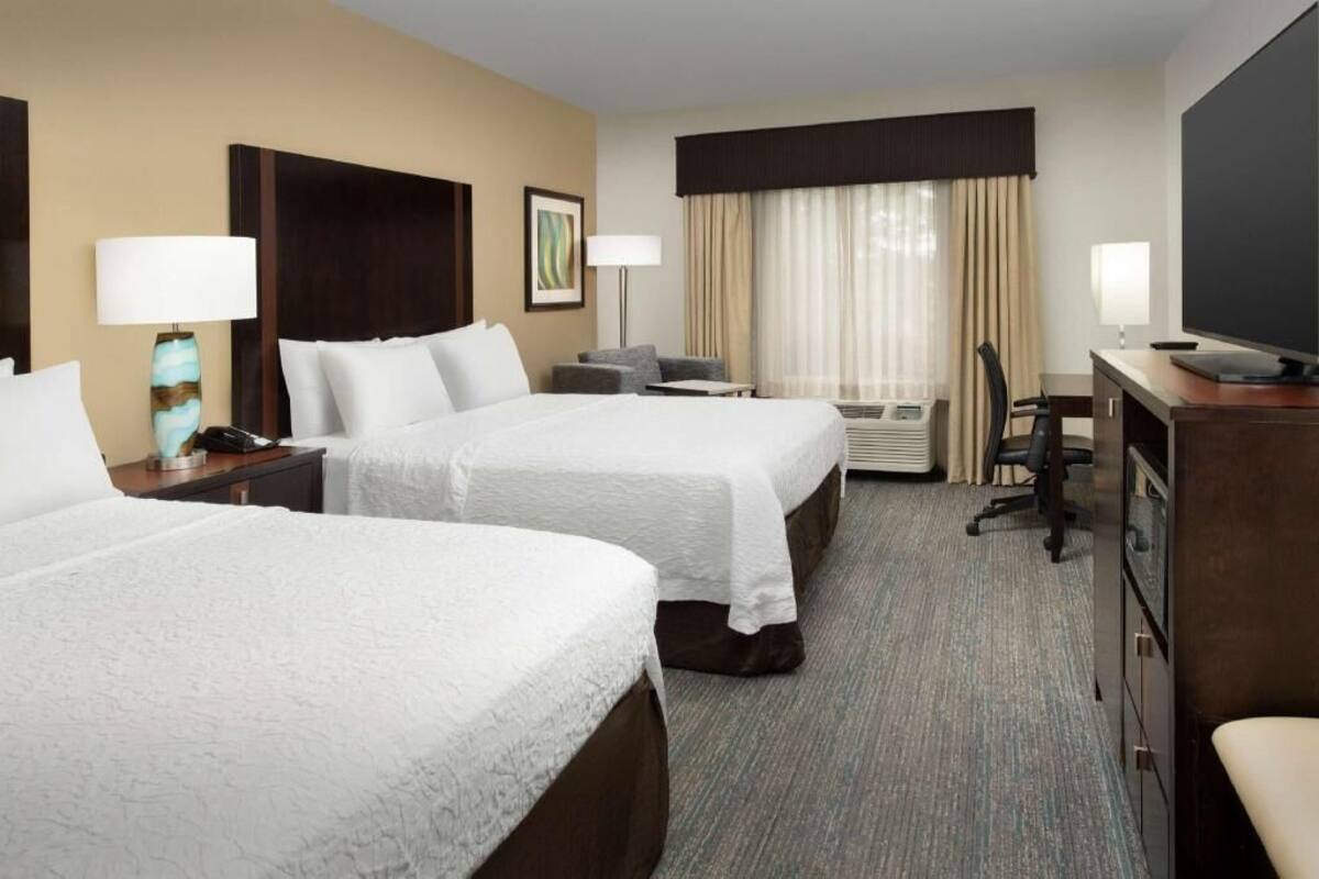 A hotel room with two beds, a desk, a chair, a television, and a window with curtains.