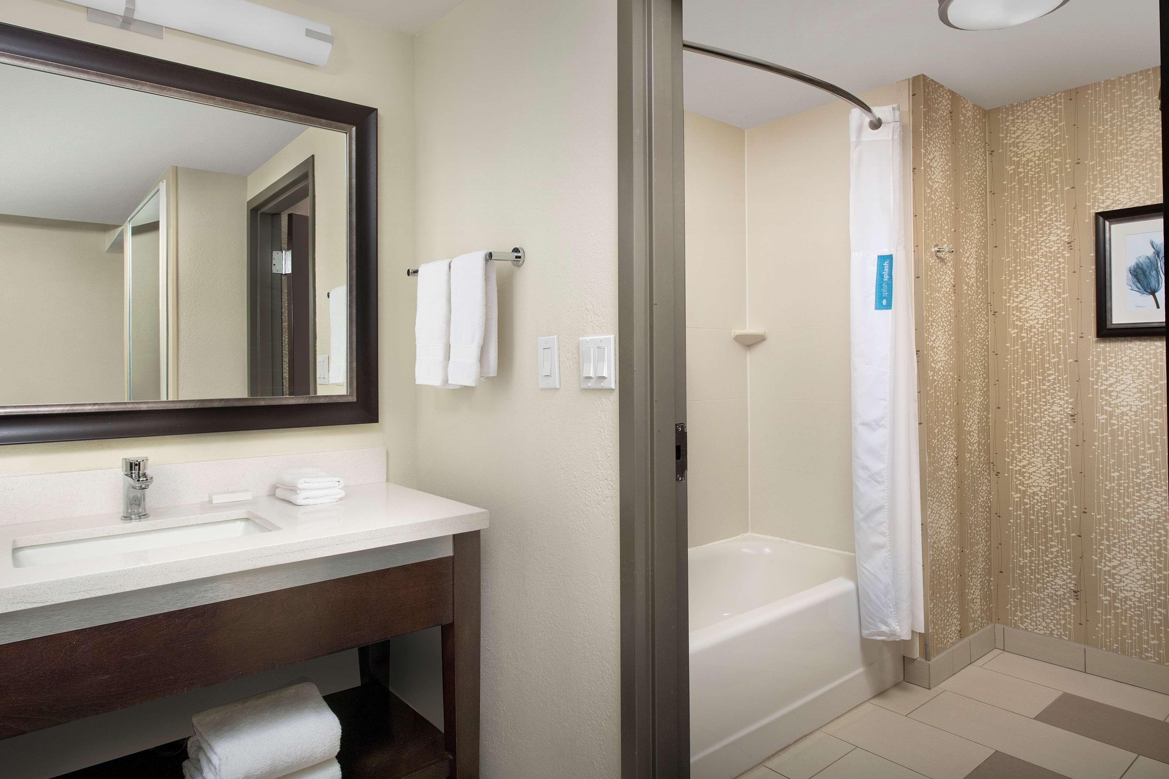 A modern bathroom with a large mirror, a sink, a bathtub, and a shower curtain.