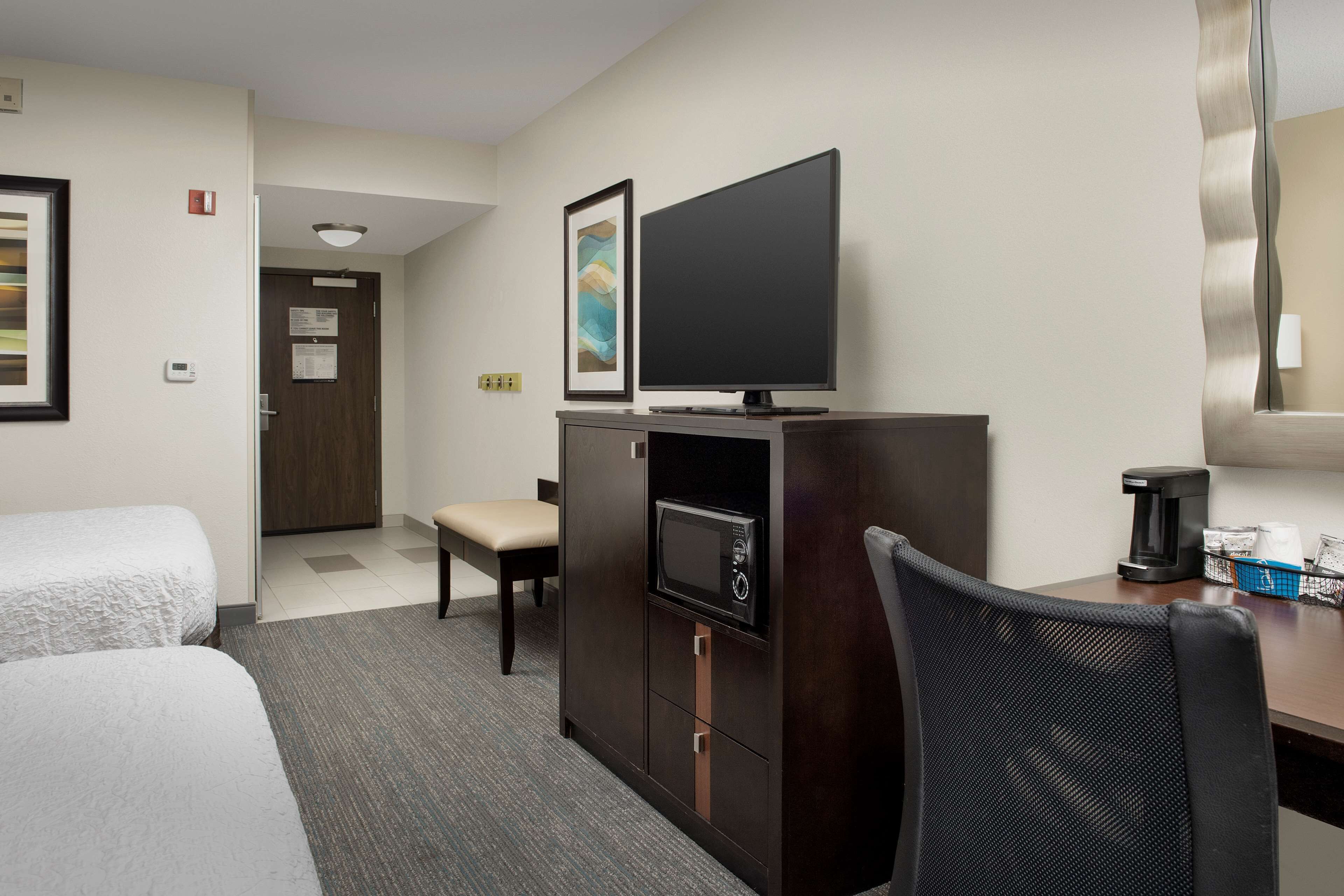 Ett hotellrum med två sängar, ett skrivbord med en kaffebryggare, en TV och en mikrovågsugn.