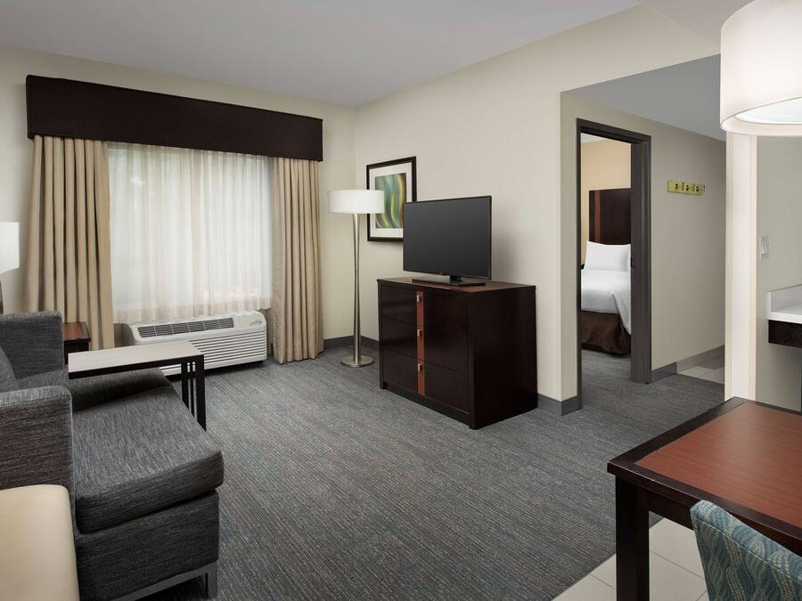 A hotel room with a sofa, a TV on a wooden stand, a desk, and a bed in the adjacent room.