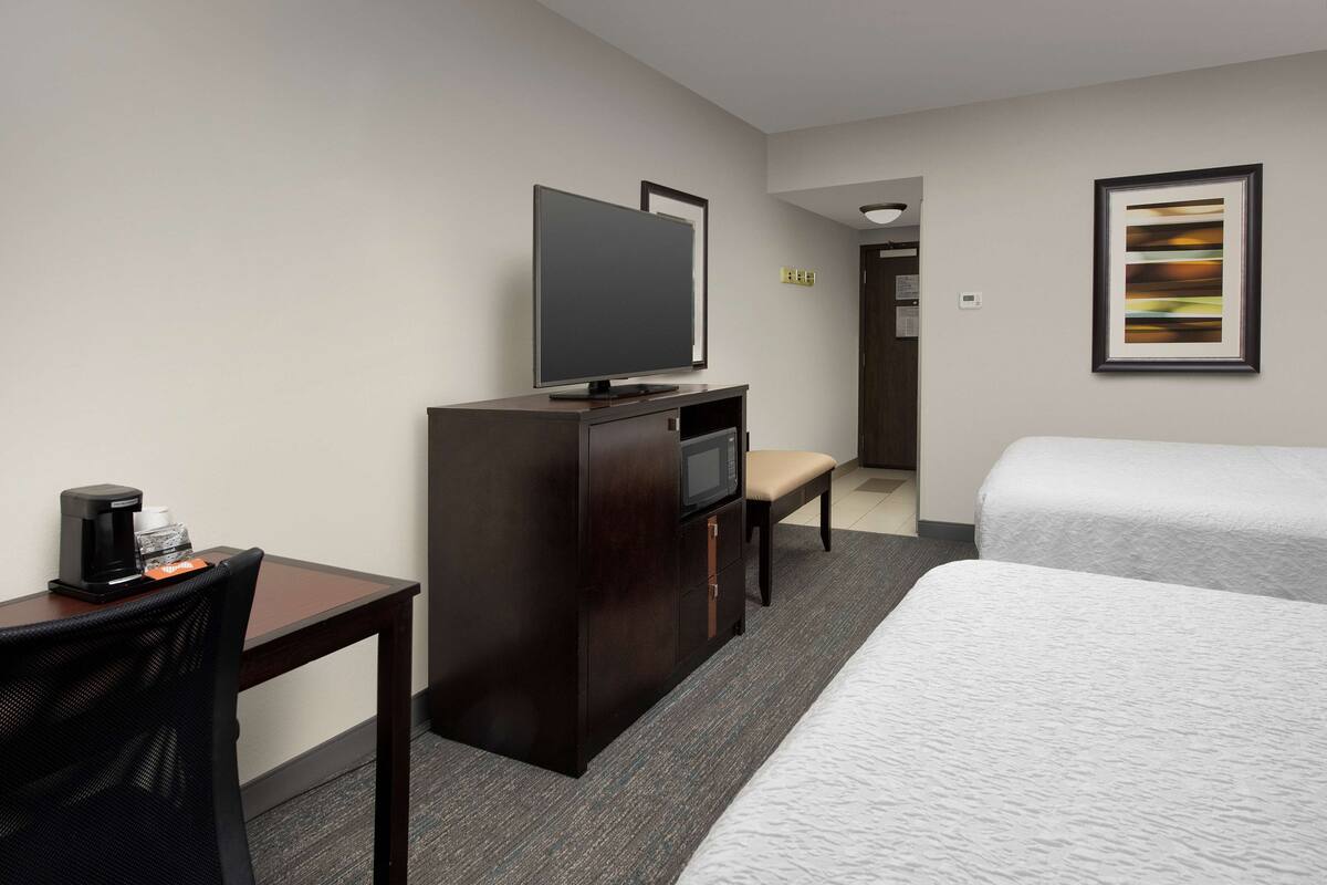 A hotel room with a bed, a desk with a coffee maker, a TV, and a framed picture on the wall.