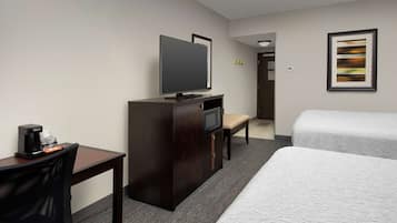 A hotel room with a bed, a desk with a coffee maker, a TV, and a framed picture on the wall.