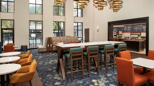 A hotel lobby with a long communal table, multiple chairs, and a bar area. - Hampton Inn & Suites Alpharetta (Alpharetta)