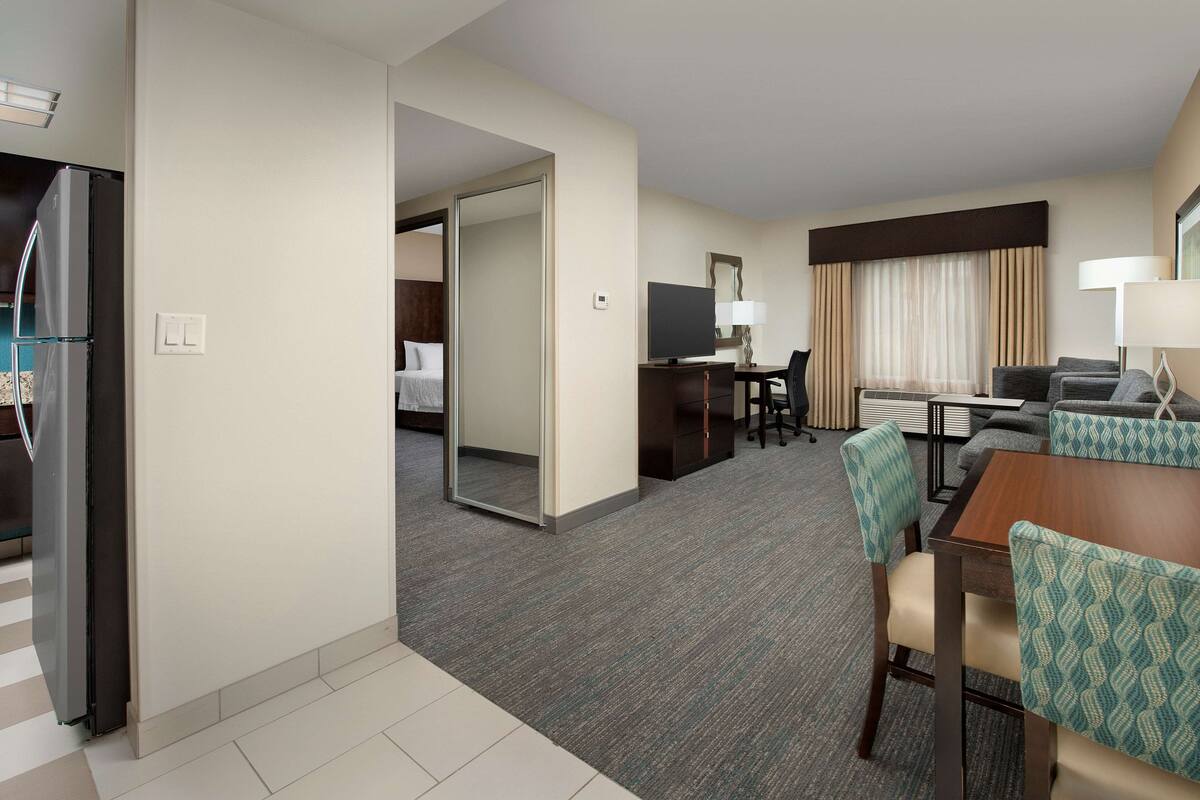 A hotel room with a kitchenette, a dining area with a table and chairs, a TV, and a bed.