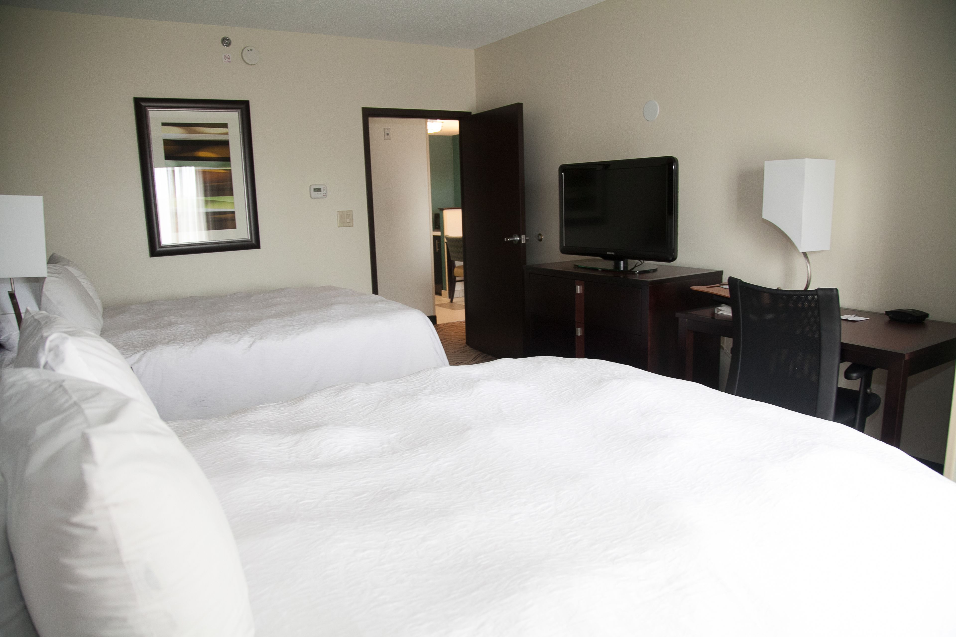 A hotel room with two beds, a television, a desk, and a chair.