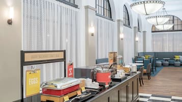 Zona de buffet con piso a cuadros, mostrador con alimentos y un cartel que dice "HAPPY BREAKFAST STARTS HERE".