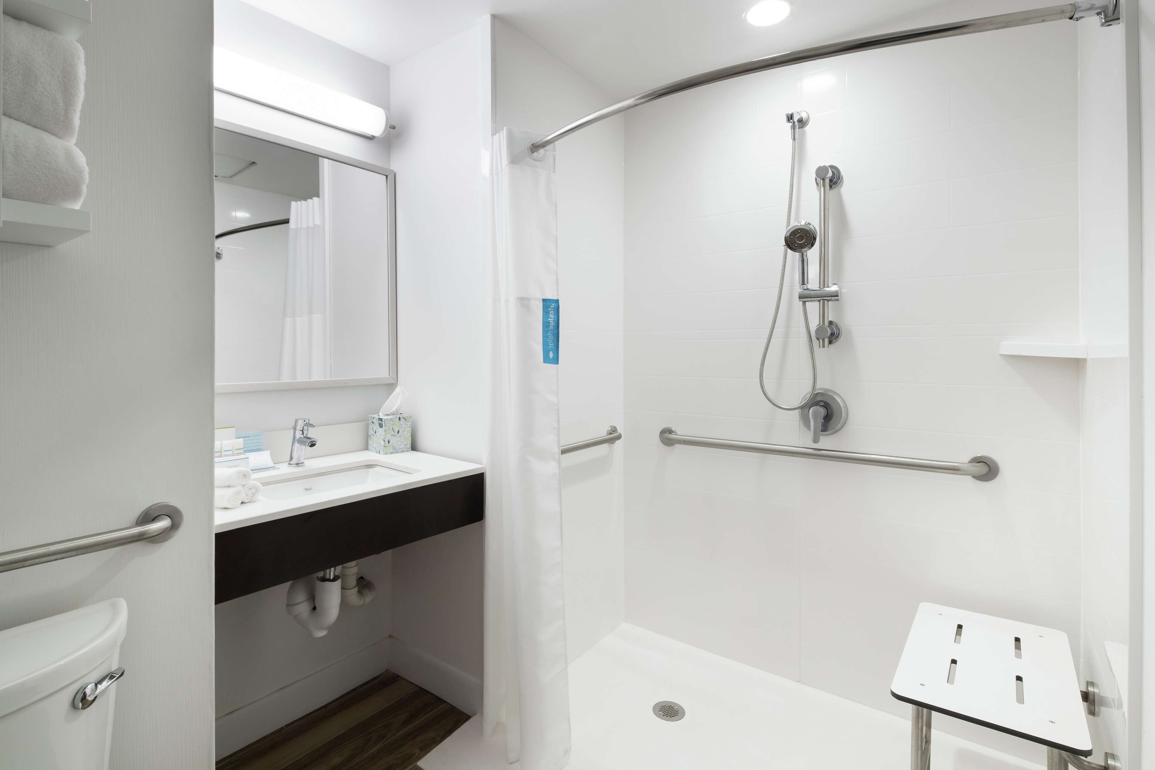 A modern bathroom with a shower, toilet, sink, and a mirror.