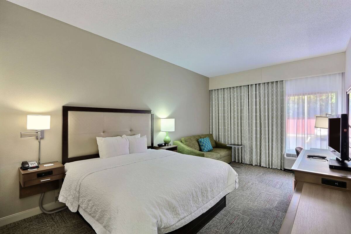Ein Hotelzimmer mit einem großen Bett, einem Schreibtisch, einem Sessel, einem grünen Sofa und einem Fernseher.