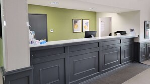 A reception area with a dark wooden counter, green walls, and framed artwork. - Super 8 by Wyndham Aurora/Naperville Area (Aurora)