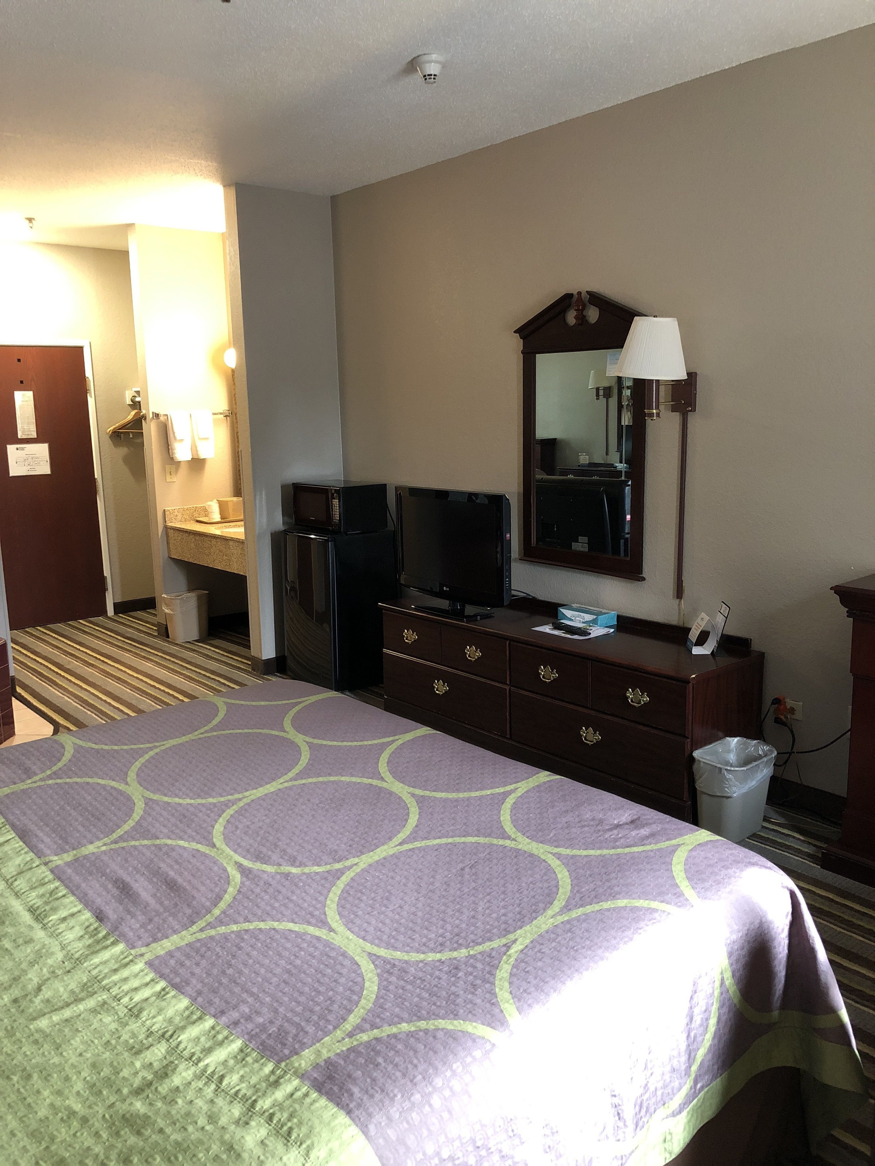 Quarto de hotel com cama, penteadeira, televisão, espelho e abajur.