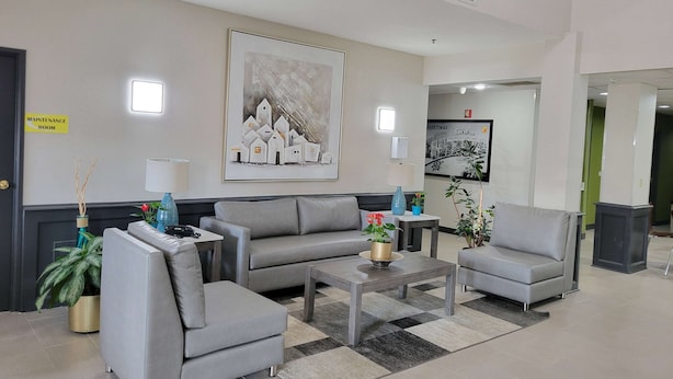 A modern lobby with a grey sofa, armchairs, a coffee table, and a painting on the wall. A maintenance room sign is visible. - Super 8 by Wyndham Aurora/Naperville Area (Aurora)