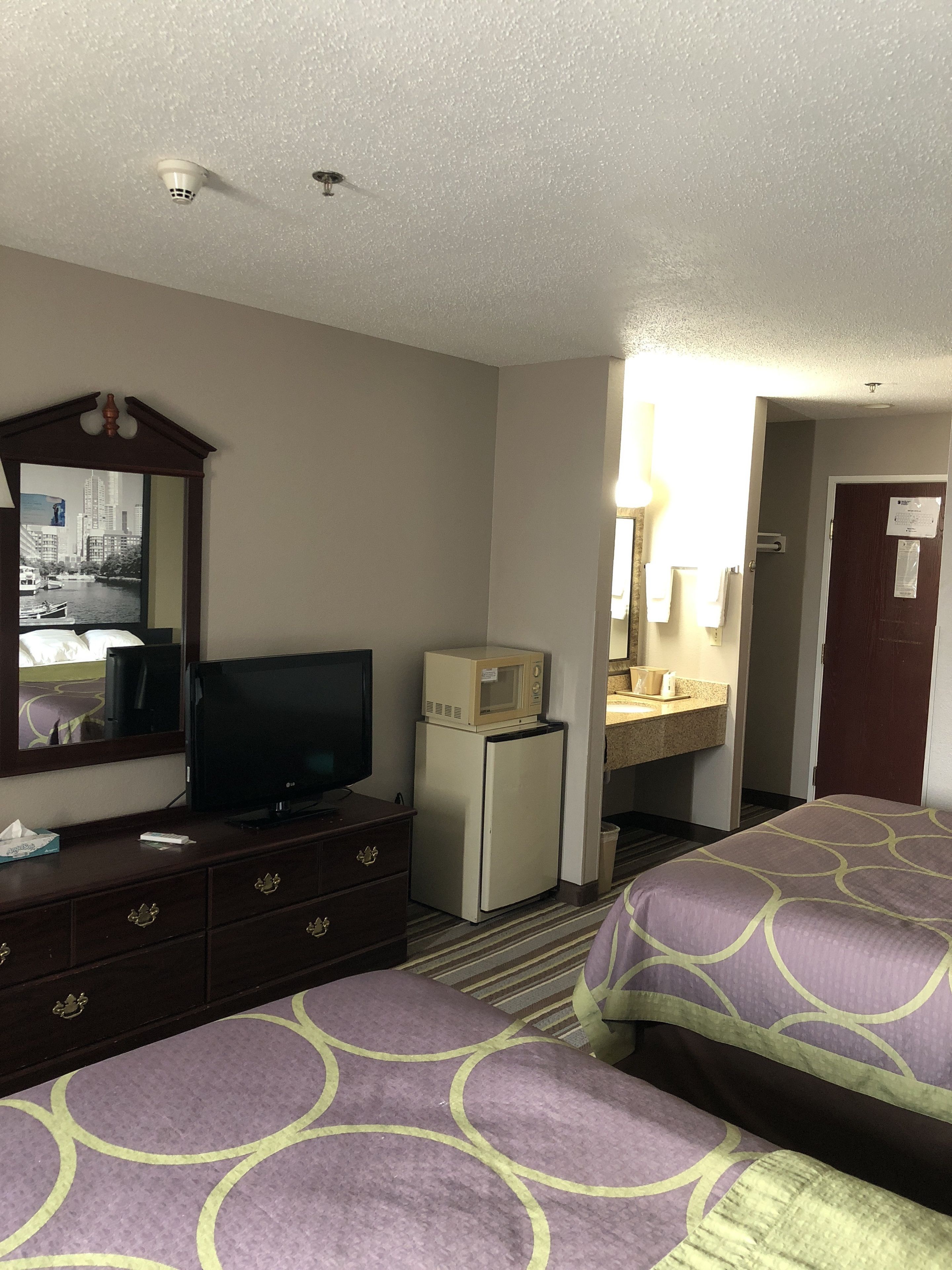 A hotel room with two beds, a television, a refrigerator, a mirror, and a bathroom visible through an open door.