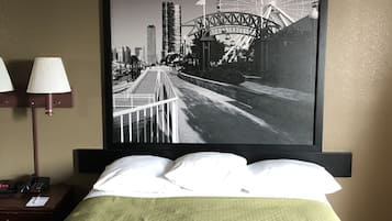 Una habitación de hotel con una cama, una mesita de noche con lámpara y un cuadro enmarcado con una vista urbana.