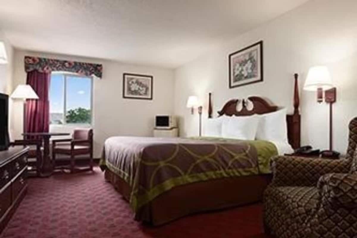 A hotel room with a bed, a desk, a chair, a TV, and a window with curtains.