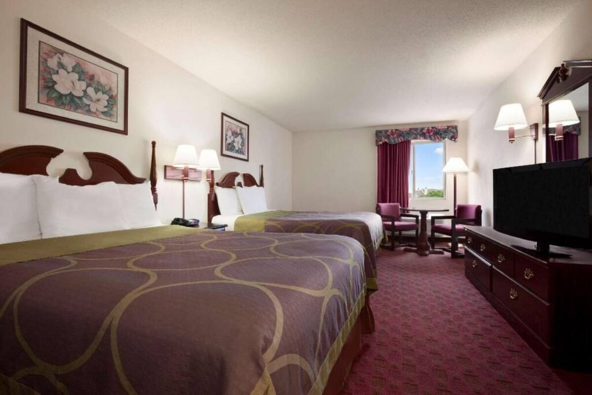 Habitación de hotel con dos camas, televisión, escritorio y ventana con cortinas.