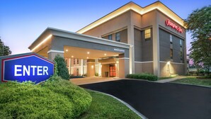 Une entrée d’hôtel moderne avec une pancarte « Bienvenue », une autre indiquant « Entrée » et une troisième portant le nom « Hampton Inn ».
