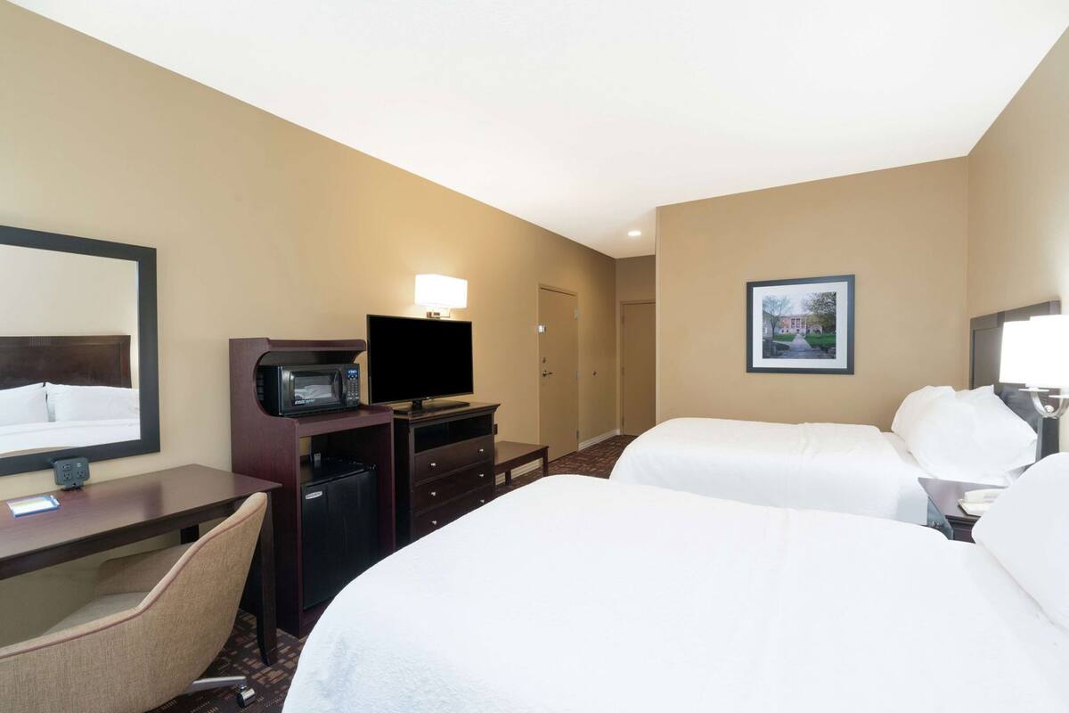 Ein Hotelzimmer mit zwei Betten, einem Schreibtisch mit Computer, einer Mikrowelle und einem Fernseher.