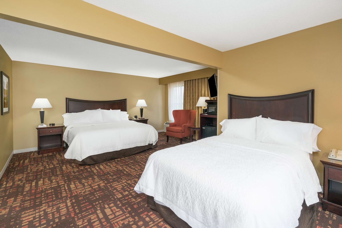 Quarto de hotel com duas camas, uma escrivaninha, uma cadeira e uma televisão.